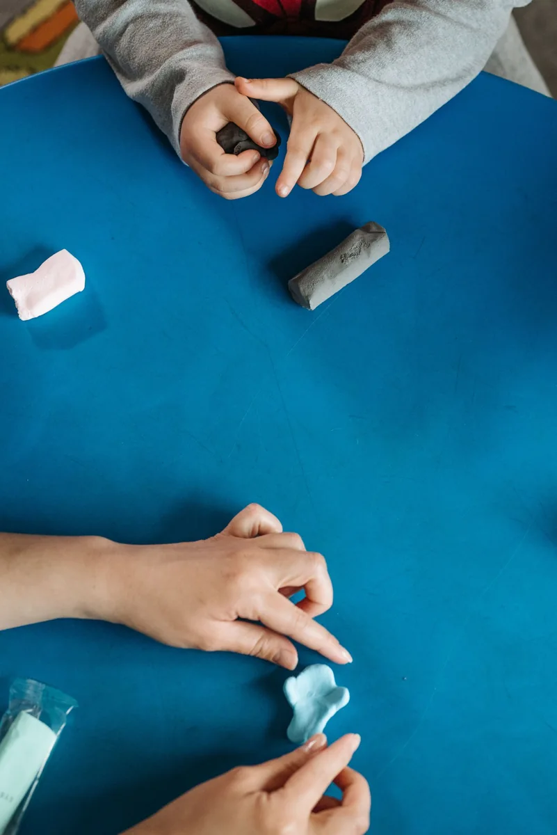Hands shaping modelling clay on a blue table
